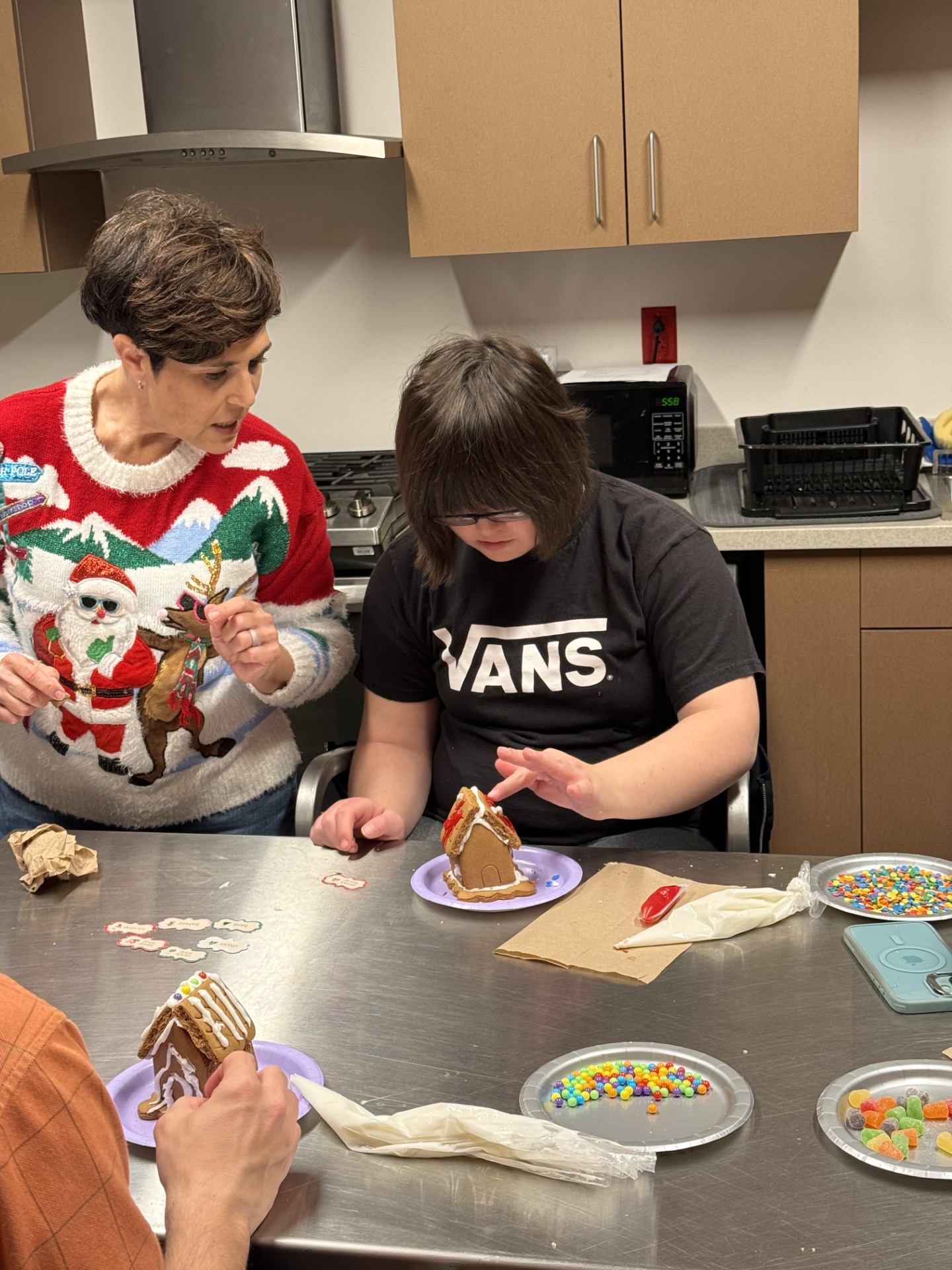 People decorating gingerbread houses with icing and candies in a kitchen.