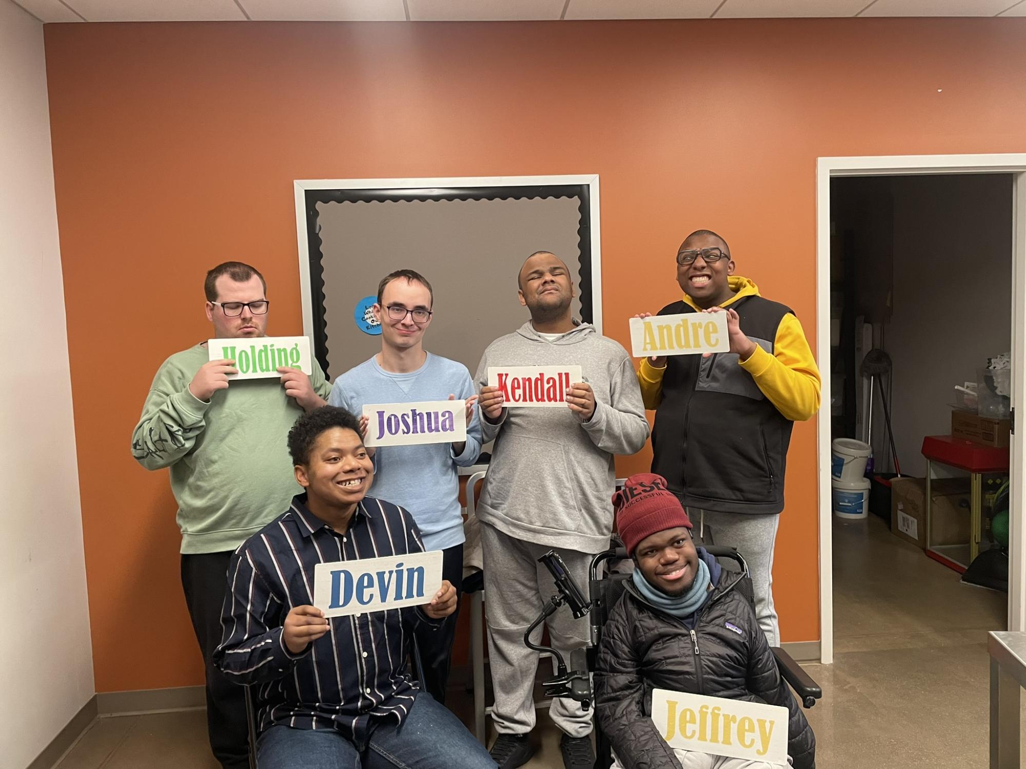 A group of six people holding name signs, with four standing and two seated in front.